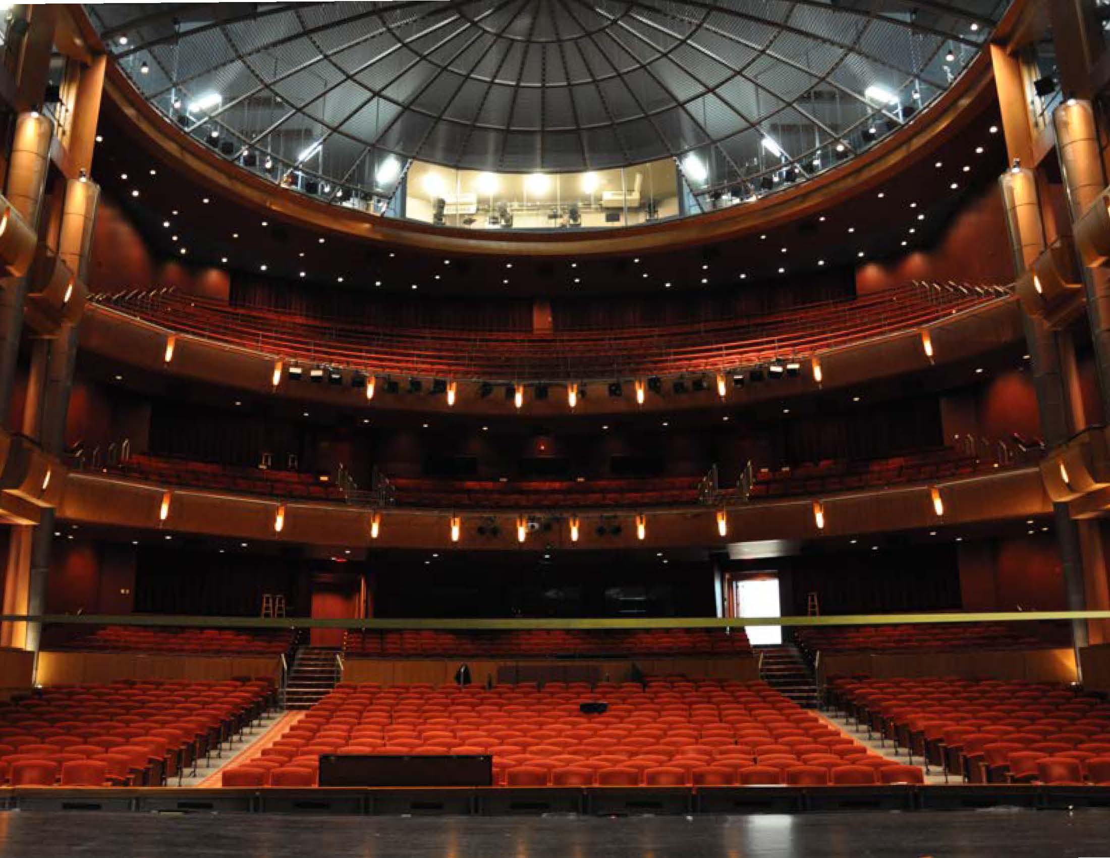 Interior of a large theater auditorium with red seats, multiple balconies, and a domed ceiling.